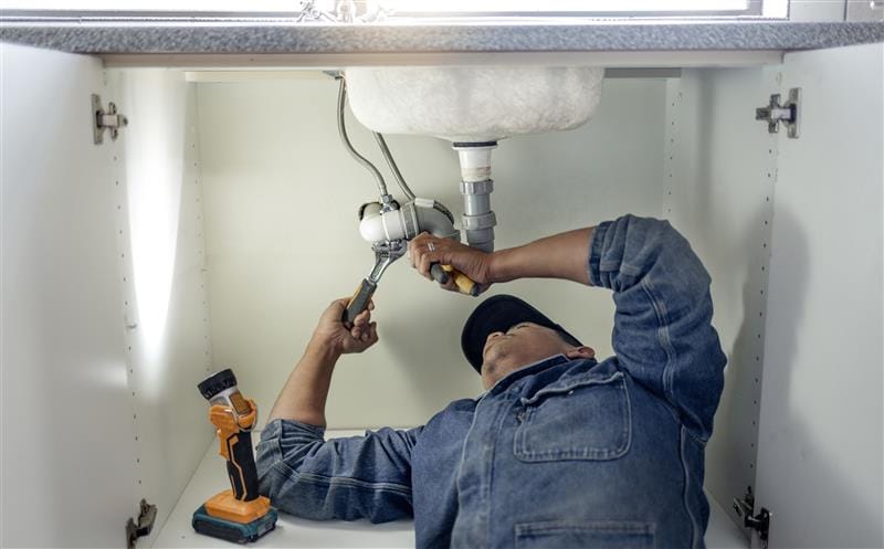 Plumber repairing pipes beneath a bathroom sink in Longmont