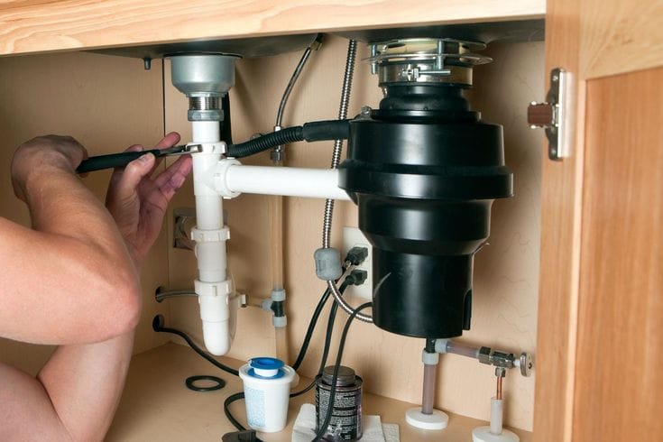 Plumber installing a garbage disposal beneath a kitchen sink in Longmont