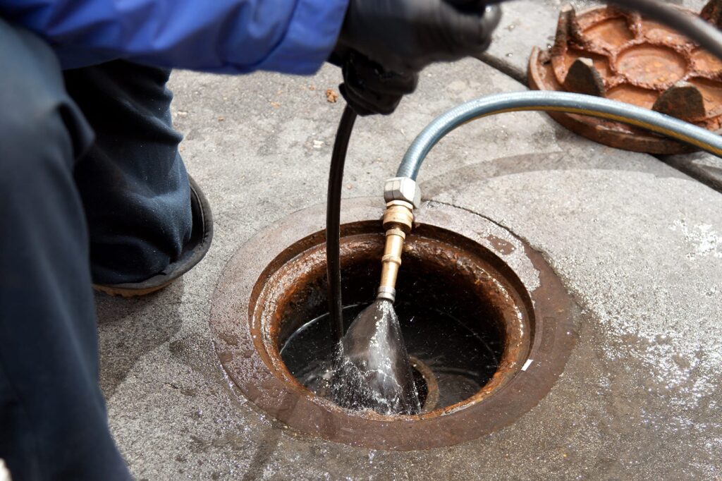 Plumber hydro jetting a sewer line through a manhole in Longmont