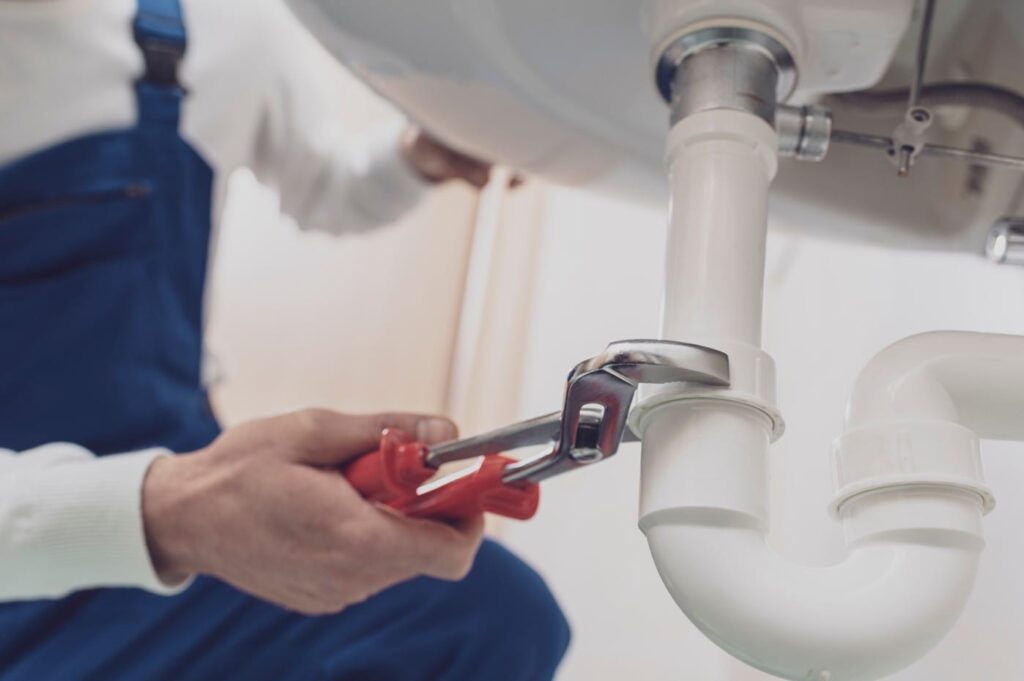 Plumber repairing a white drain pipe beneath a sink in Longmont