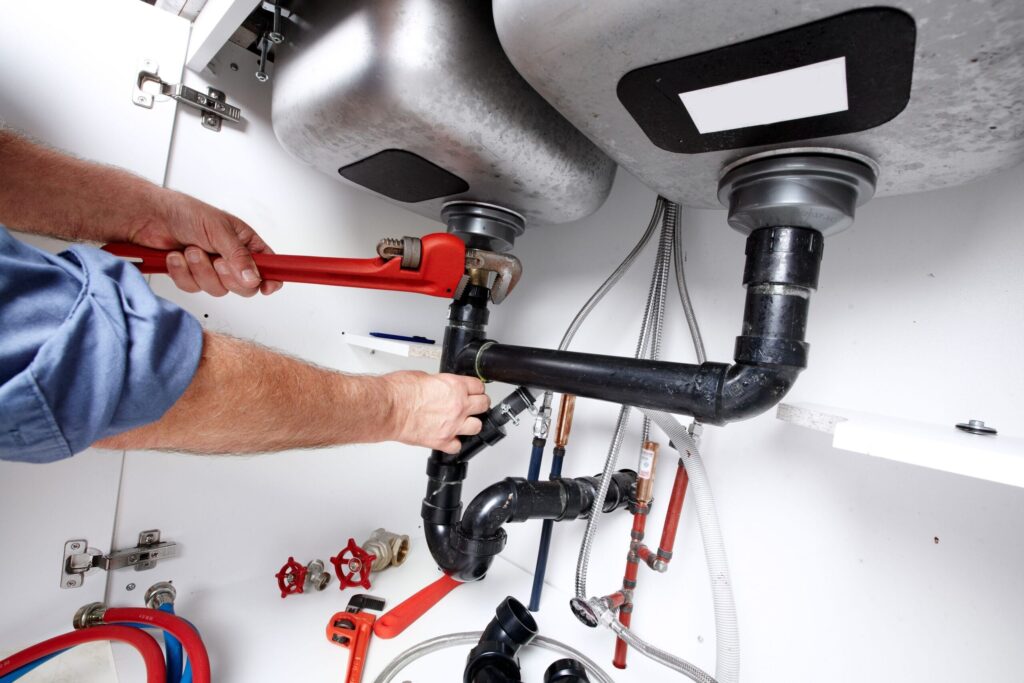 Plumber repairing drain pipes beneath a kitchen sink in Longmont